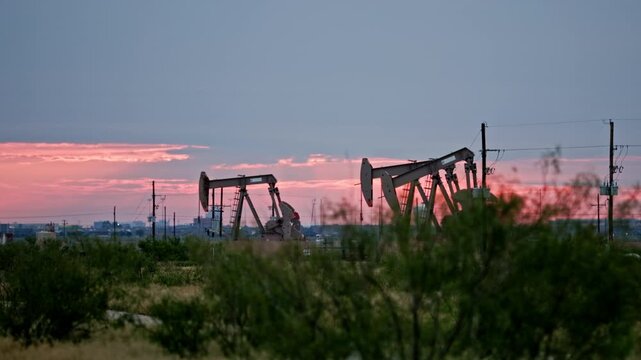 Pump Jacks Pumping in Desert Field Outside of City during Early Morning Sunrise