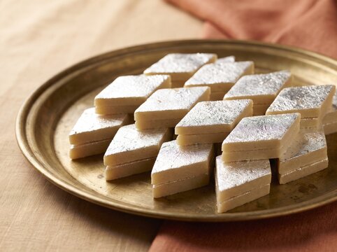 Delicious kaju katli sweets arranged neatly on a traditional brass plate with warm lighting