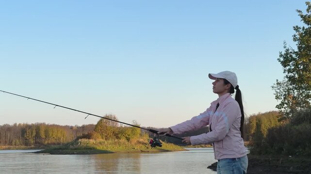 Woman in a cap holding a fishing rod beside calm autumn water