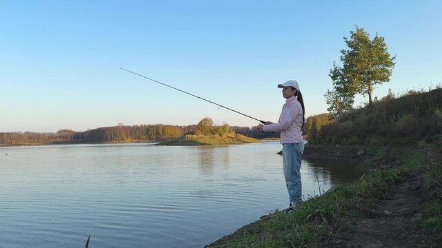 Woman fishing on a quiet shore with autumn trees and blue sky