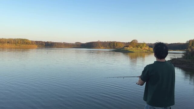 Rear view of a man fishing beside calm water in autumn