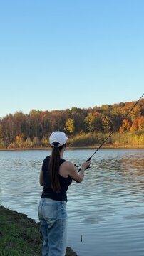 Woman fishing beside calm water with golden autumn trees