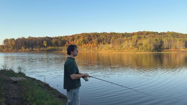Man fishing from the shore with autumn forest across the water