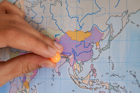 A hand placing an orange thumbtack on a map of Asia, pointing to the area of ​​Burma