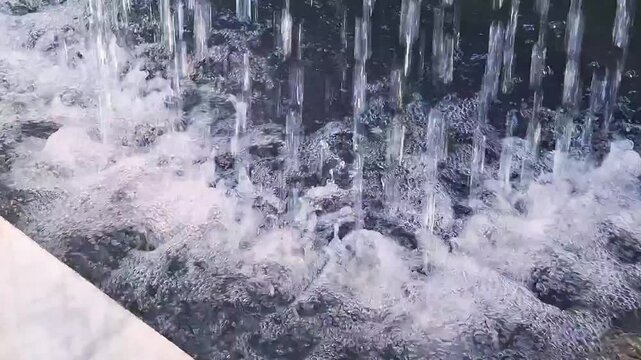 High angle view of cascading water jets crashing into stone basin pool beside marble ledge creating intense white foam
