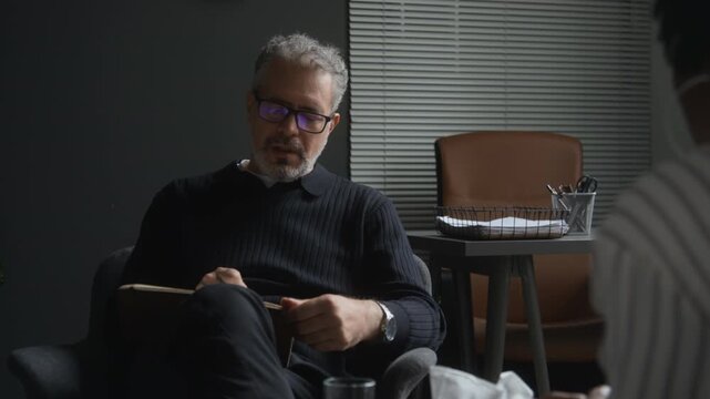 Middle aged Caucasian male psychologist gesturing during psychotherapy consultation with patient. Suitable for mental health awareness campaigns and medical therapy advertisements