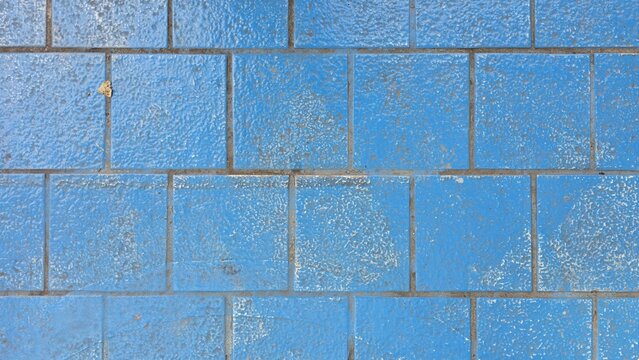 Old blue concrete pavers with faded and stained texture. Top view grid pattern of weathered blue cement flooring showing paint chipping. Abstract weathered blue grid pattern on concrete pavement.