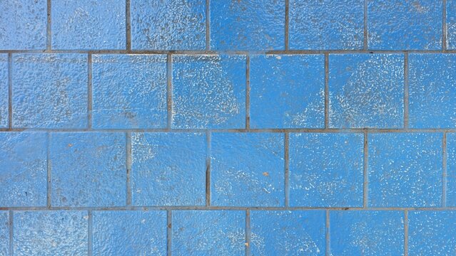 Old blue concrete pavers with faded and stained texture. Top view grid pattern of weathered blue cement flooring showing paint chipping. Abstract weathered blue grid pattern on concrete pavement.
