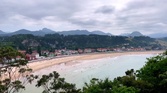 panoramic view of sandy beach coastal town and mountains under cloudy sky- Ribadesella, Asturias in Spain
