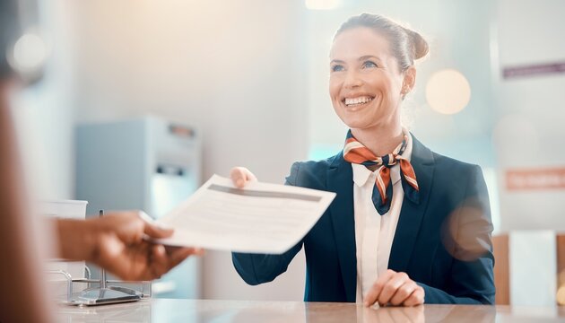 Smiling female customer service agent in uniform assists a passenger with travel documents at the reception counter