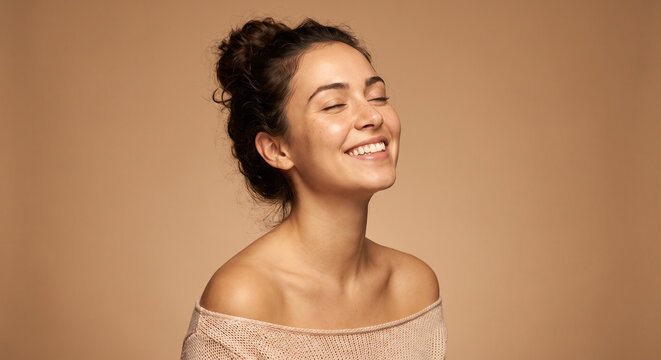 Happy young woman smiling with eyes closed and bare shoulders displaying natural radiant skin and a glowing complexion during her daily beauty and skincare routine