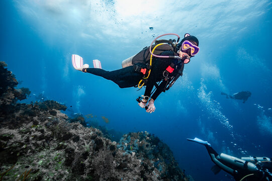 Playful female scuba diver exploring a deep blue coral reef
