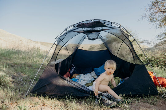 Cute toddler in a diaper sits inside a camping tent