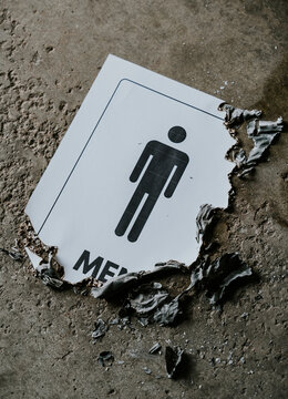 Partially burned mens restroom sign on concrete floor