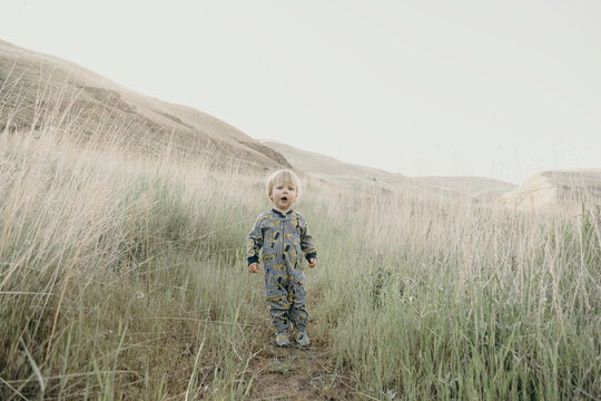 Toddler boy in pajamas stands on a path in a grassy field
