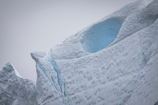 A massive sculpted iceberg against an overcast sky