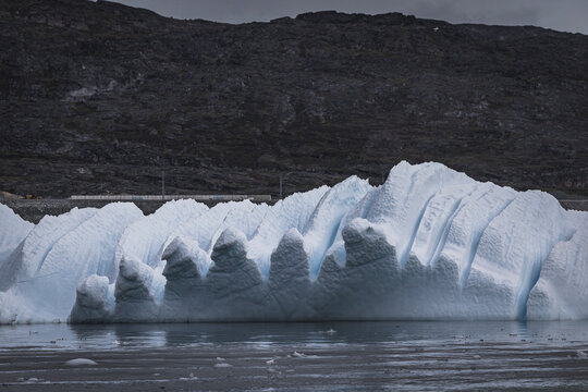 A massive sculptural iceberg floats past a rocky coastline