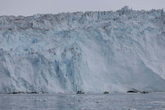 Small tourist boats dwarfed by massive glacier wall