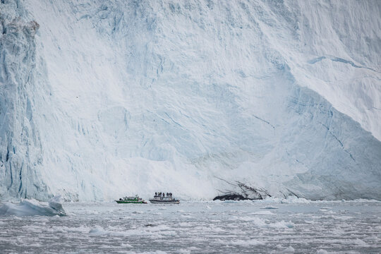 Two small tour boats float before massive glacier wall