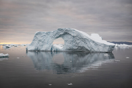 Large iceberg with a natural arch in calm ocean water