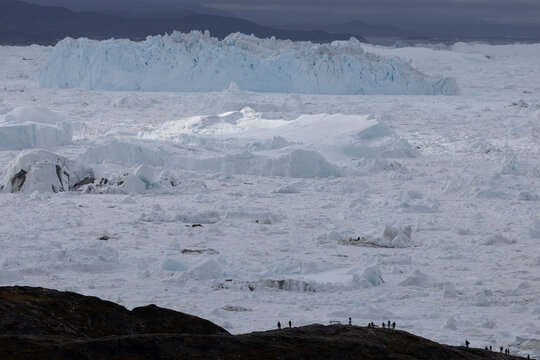 Silhouetted people watch a massive arctic glacier