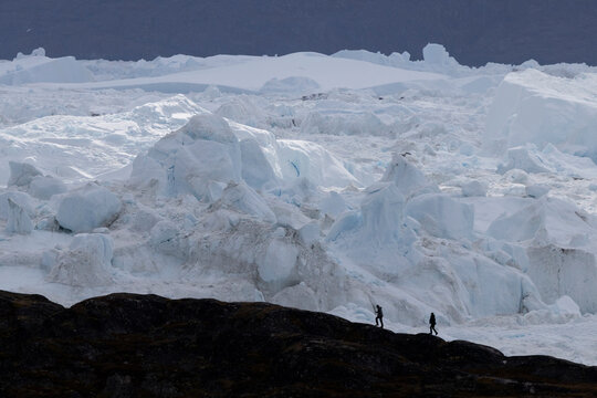 Two hikers walk on a ridge above a massive glacier