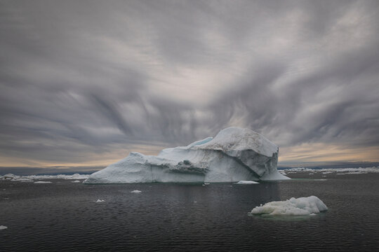 Large iceberg floats in arctic waters under dramatic clouds