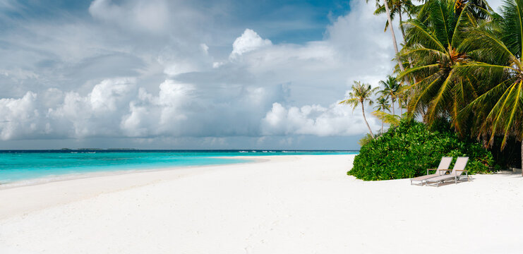 Panoramic view of tropical beach with white sand, palm trees, turquoise ocean water and blue cloudy sky