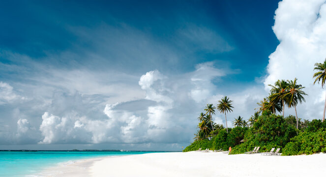 Panoramic view of tropical beach with white sand, palm trees, turquoise ocean water and blue cloudy sky