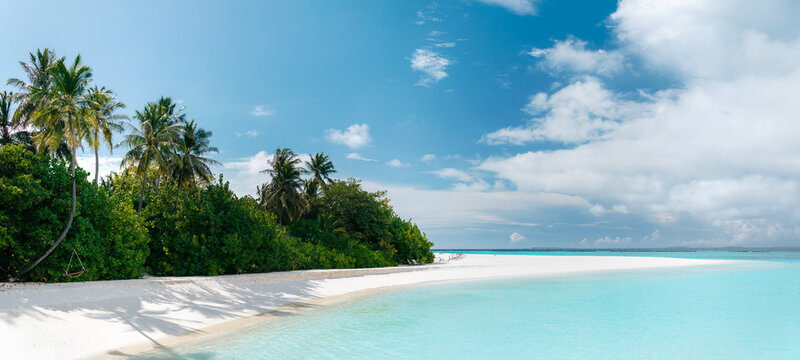 Panoramic view of tropical beach with white sand, palm trees, turquoise ocean water and blue cloudy sky