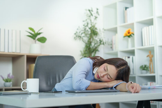 Asian businesswoman sleeping at office desk from exhaustion and office syndrome