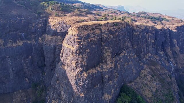 A drone video of majestic view of a rugged sunlit cliff side towering over deep mountain valleys