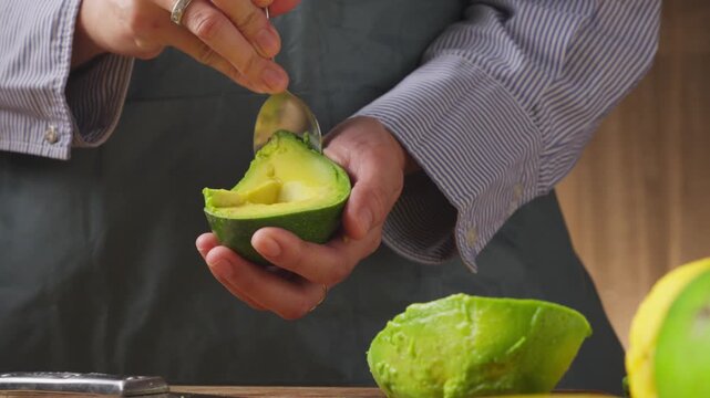 Scooping creamy ripe avocado flesh from the skin with a spoon