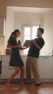 Young couple receiving great news on a laptop celebrating with a high five and dancing with joy in the kitchen while feeling happy, excited, and triumphant. Vertical video