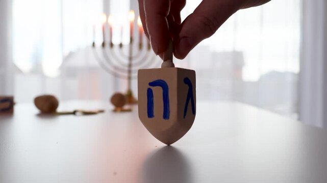 Hands arrange wooden Hebrew letter blocks in front of a glowing Hanukkah menorah indoors