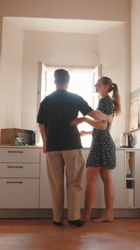 Romantic young couple hugging, kissing, and dancing together in a sunlit kitchen, embracing each other with love and affection in a cozy apartment, enjoying a happy moment. Vertical video