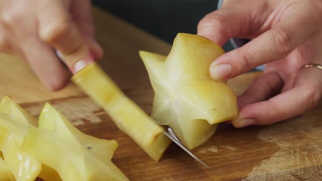 Person cutting a fresh ripe yellow starfruit, with a kitchen knife, closed up