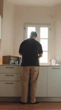 Man doing dishes in a modern kitchen while looking out the window, enjoying a tranquil moment of daily life and embracing the simplicity of household chores in the sunlight. Vertical video