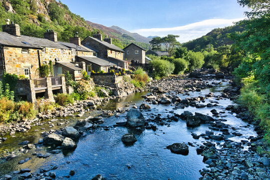 Beddgelert village in Snowdonia, Wales, with traditional stone cottages beside a rocky river and dramatic mountain scenery.