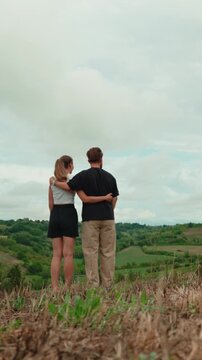 Romantic couple embracing on a hill, enjoying the scenic green valley view. Young man and woman on a date in nature, showing love, affection and connection. Vertical video 