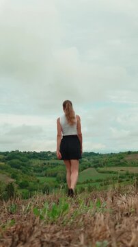 Barefoot young woman walking in a scenic green field stopping to raise her arms, celebrating freedom, success, and connection with nature in the countryside. Vertical video 