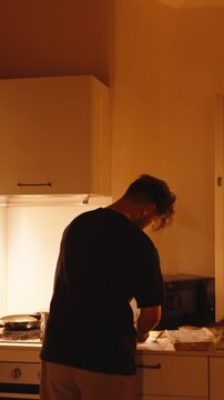 Young man preparing a meal in a warmly lit kitchen at night, showcasing his cooking skills and the intimate atmosphere of home life during a quiet evening routine. vertical video 