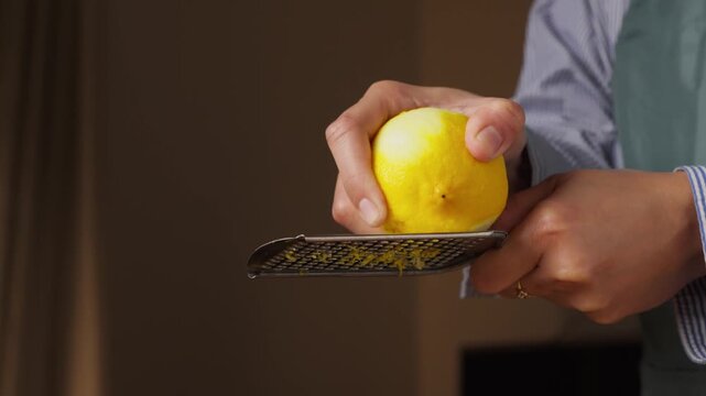 Hands grating the outer peel of a fresh yellow lemon with a fine handheld grater