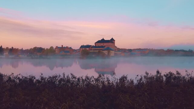 Panning castle behind lake or river canal with reeds in foreground, sunrise in Finland H&auml;meenlinna