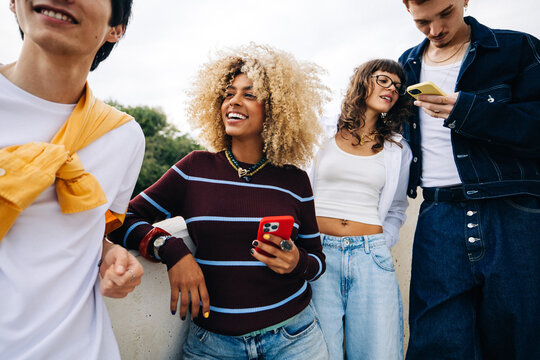 Young friends socializing outdoors while smiling with phones