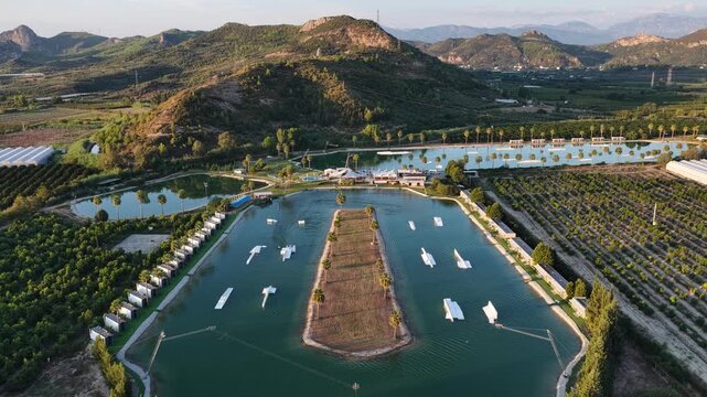 World class wakepark in Antalya, Turkey, with riders on crystal clear lakes surrounded by palm trees and mountains and multiple water obstacles for wakeboarding. Cable Wake park in Turkey.