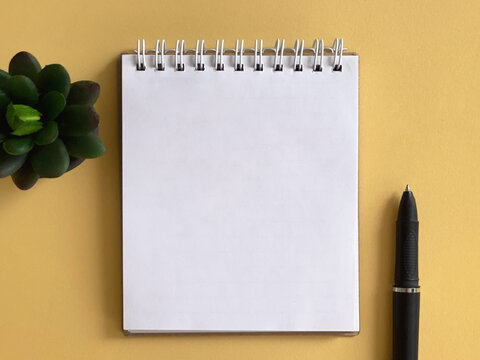 Blank spiral notebook with black pen on yellow background, minimalist workspace concept for writing, planning, creativity and productivity.