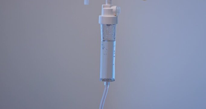 A high-quality stock video clip of an intravenous (IV) drip in a clinical setting. The camera focuses on a transparent IV fluid bag connected to sterile tubing, with saline solution droplets.