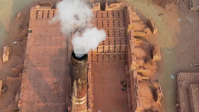 A traditional brick-making yard in Bangladesh with stacks of clay bricks and a chimney emitting smoke above the production area - drone shot