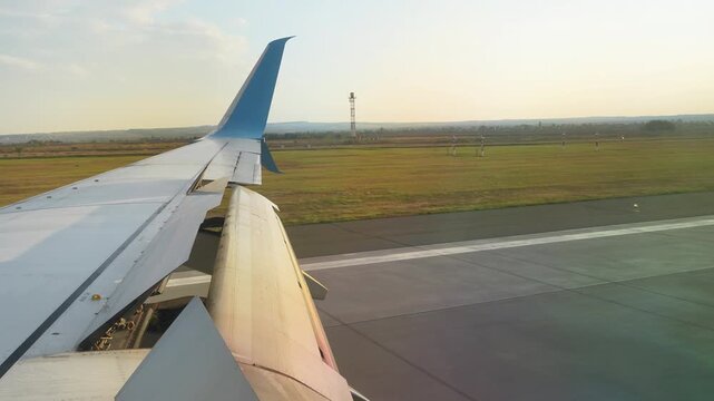 Commercial passenger airplane wing with open flaps during taxiing on an airport runway tarmac outdoors. Beautiful aviation background template for travel, tourism, vacation trip, international flight.